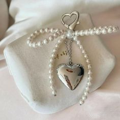 a white bag with pearls and a heart charm on it's side, sitting on a bed