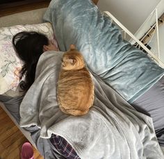 an orange cat laying on top of a bed next to a woman