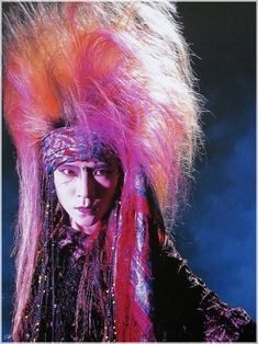 a woman with colorful hair and makeup on her face, wearing an elaborate headdress