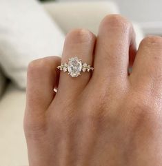 a woman's hand with a diamond ring on top of her finger, in front of a couch