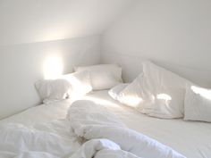 an unmade bed with white sheets and pillows