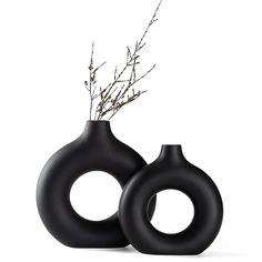 two black vases sitting next to each other on a white surface with branches in them