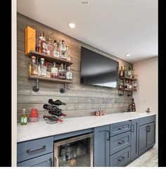 a kitchen with blue cabinets and shelves filled with liquor bottles next to a flat screen tv mounted on the wall