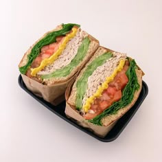 a sandwich with lettuce, tomato and mayonnaise on it sitting on a black tray