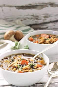 two bowls filled with soup on top of a wooden table next to silver spoons