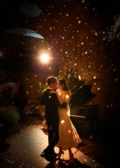 a man and woman standing next to each other in front of a piano at night