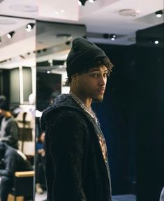 a young man standing in front of a mirror wearing a black jacket and hat with his hands in his pockets