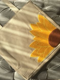 a yellow sunflower on a tan pillow with a brown circle in the center and an orange dot at the bottom