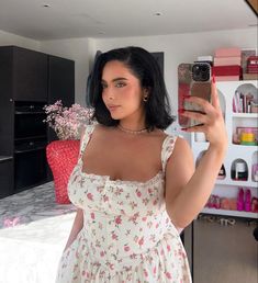 a woman taking a selfie with her cell phone in the kitchen and wearing a floral dress