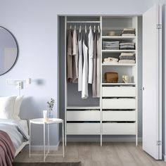 a white closet with drawers and clothes hanging on the doors, next to a bed