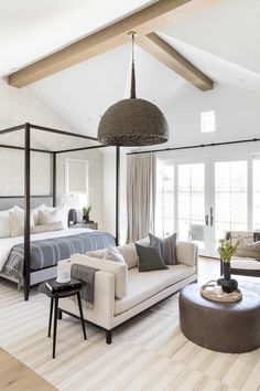 a bedroom with white walls and wood floors has a four poster bed, two couches, a coffee table, and a chandelier