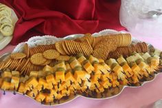 a platter filled with crackers and cheese on top of a pink table cloth