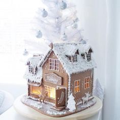 a gingerbread house with a lit up christmas tree on the top and snow covered roof