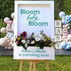 a baby shower sign with balloons and flowers in the back ground at a baby shower