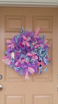 a purple and pink wreath hanging on the front door of a house with ladybug buttons