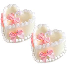 two heart shaped cakes with bows and pearls on the sides, one is white and the other is pink