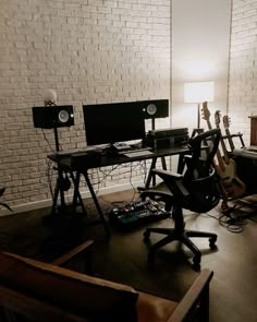 a room with two computers and guitars on the desk, in front of a white brick wall