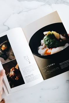 an open book with pictures of food in it on top of a marble countertop