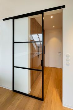 an open glass door in the middle of a room with wood flooring and white walls