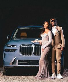 a man and woman standing in front of a car wearing formal wear, posing for the camera