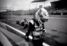 a black and white photo of a person in a racing suit on a race track