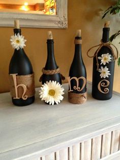 three wine bottles are decorated with daisies and burlocks to spell the word love