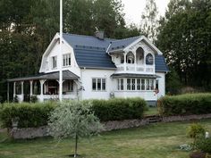 a white house with a blue roof in the middle of some trees and bushes around it