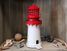 a red and white lighthouse sitting on top of a wooden shelf next to sea shells