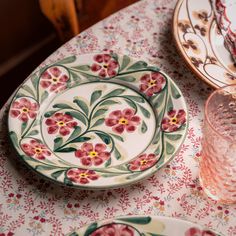 a table topped with plates and glasses on top of a white tablecloth covered in red flowers