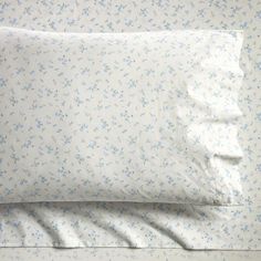 two pillow cases sitting next to each other on top of a bed covered in white sheets and blue flowers