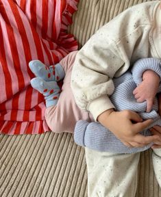 a baby laying on top of a couch next to a person holding a stuffed animal