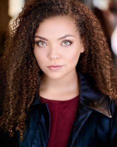 a woman with long curly hair wearing a leather jacket