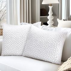 a white couch with three pillows on it in front of a window and a lamp