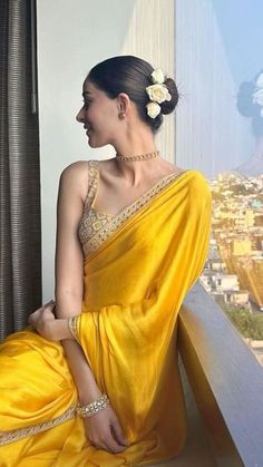 a woman in a yellow sari sitting on a window sill