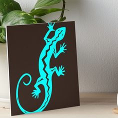 a blue gecko silhouette on a black and brown background art board with a plant next to it