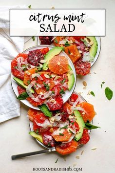 two plates filled with sliced oranges and avocado on top of a white table