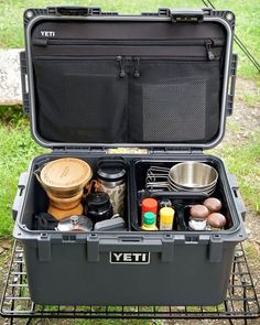 an open yeti cooler sitting on top of a grass covered field with cooking utensils in it