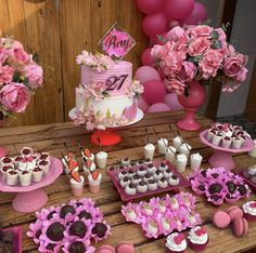 a table topped with lots of desserts and pink flowers on top of wooden tables