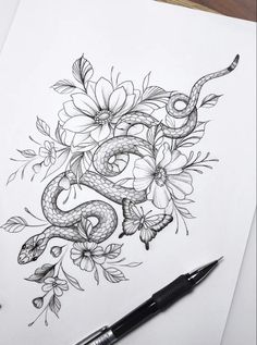 a drawing of a snake and flowers on paper with a pen in the foreground