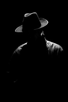 a black and white photo of a man with a hat on his head in the dark