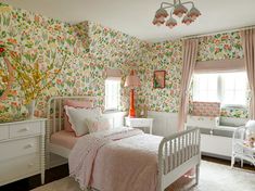 a bedroom with floral wallpaper and pink bedding, white dressers and baby's crib