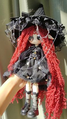 a doll with red hair is wearing a black hat and holding it in her hand