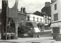 an old black and white photo of a street corner with buildings on both sides, flowers in the foreground