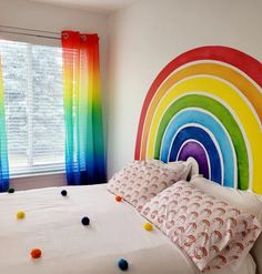 a rainbow themed bedroom with white bedding and colorful curtains