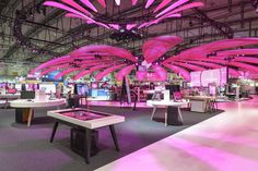 a room filled with lots of tables covered in pink umbrella like decorations and lights on the ceiling