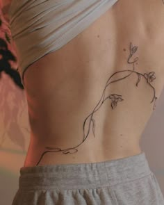 a woman's lower back tattoo with vines and flowers on her left ribcage