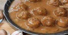 meatballs and gravy in a skillet on a wooden table next to mushrooms