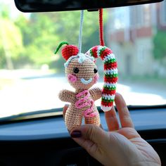 a hand holding a small stuffed animal hanging from a car dash board in front of a window