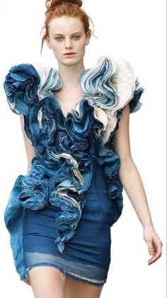 a woman is walking down the runway wearing a blue dress with ruffles on it