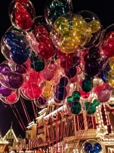 many balloons are floating in the air near a carnival ride at night with lights on